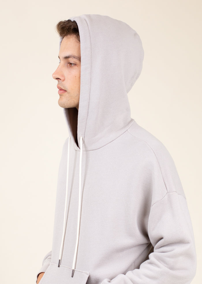 Person wearing a light gray hoodie with hood up against a beige background