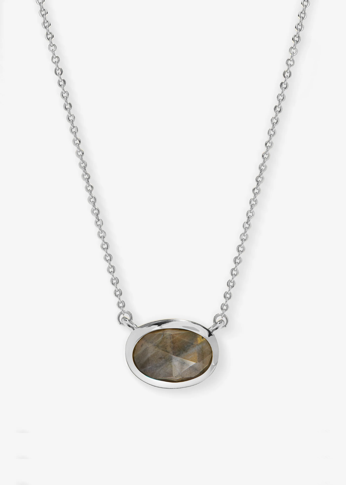 Silver necklace with a silver framed oval labradorite pendant laying on a grey background
