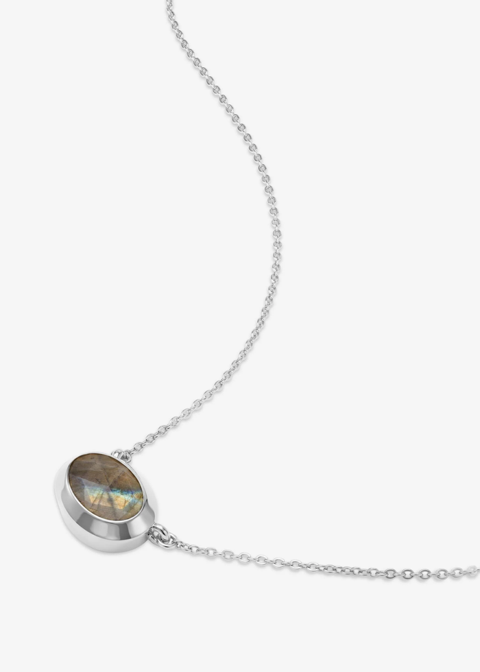 Silver necklace with a silver framed oval labradorite pendant laying on a grey background