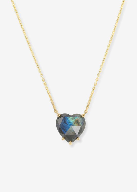 Heart shaped labradorite pendant on a gold chain necklace laying on a white background