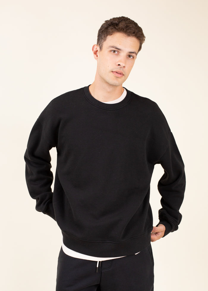 Man wearing a black crewneck sweatshirt on a beige background