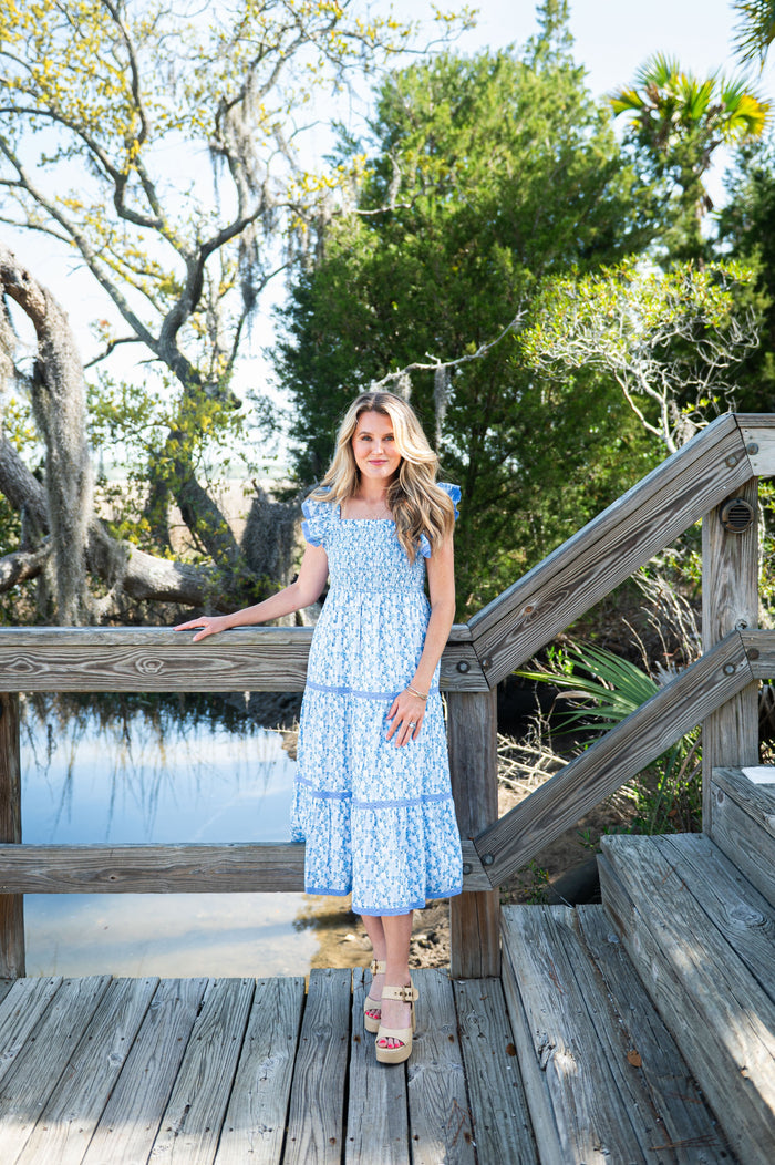 Woman in a blue dress standing on a wooden deck with trees in the background