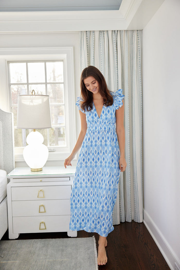 Model in a long blue ikat dress with ruching under the bust and flutter sleeves.