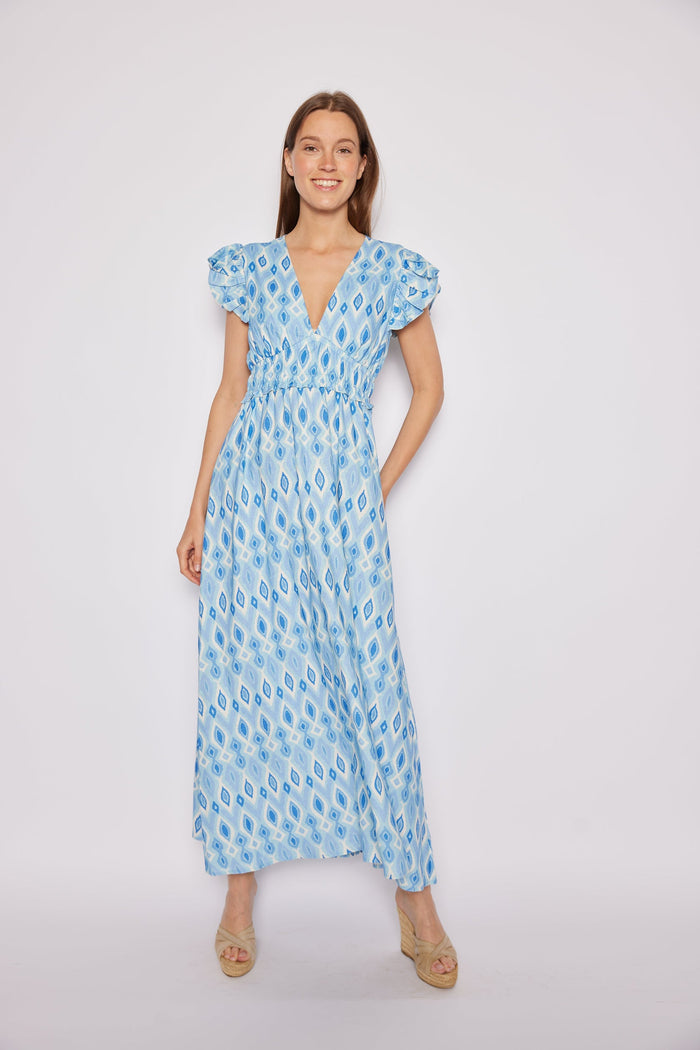 Model in a long blue ikat dress with ruching under the bust and flutter sleeves.