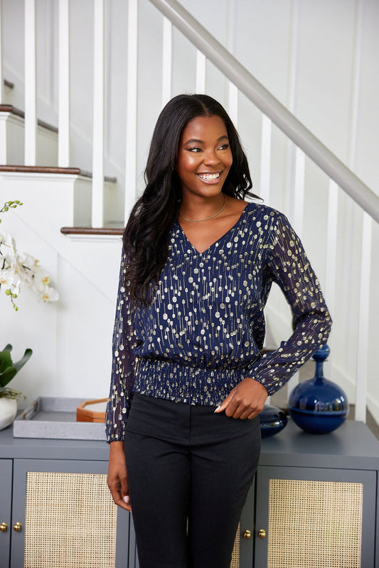 Woman in a blue patterned top and black pants standing in a home setting.