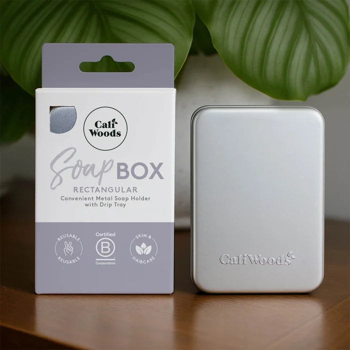 CaliWoods soap holder with packaging on a wooden surface with green leaves in the background.