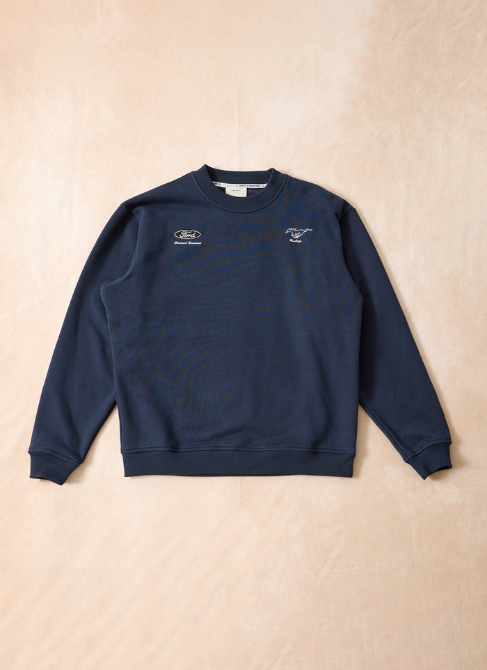 Navy blue Percival x Ford collaboration sweatshirt with white embroidered logos, laid flat on a beige surface.