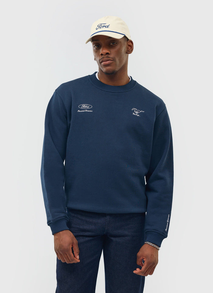 A model wears the navy Percival x Ford sweatshirt with custom embroidery, styled with dark jeans and a Ford baseball cap.