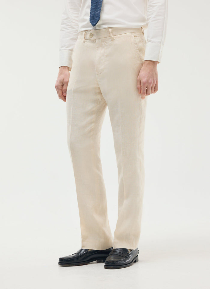 A model wears Percival's cream tailored linen trousers, a white shirt, and black loafers.