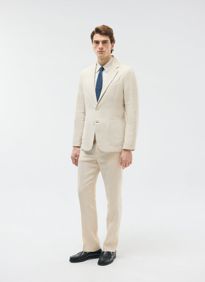 A model wears Percival's cream tailored linen trousers with a matching blazer, white shirt and blue tie.
