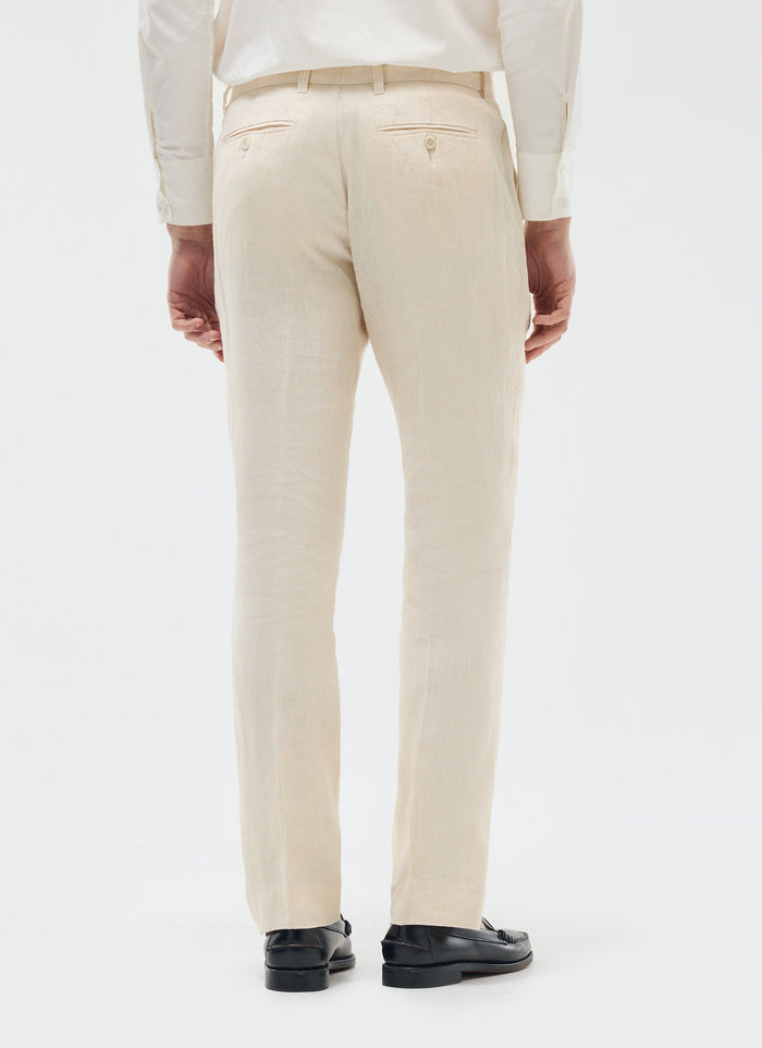 A model seen from behind wearing the Percival cream tailored linen trousers with a white shirt and black loafers.