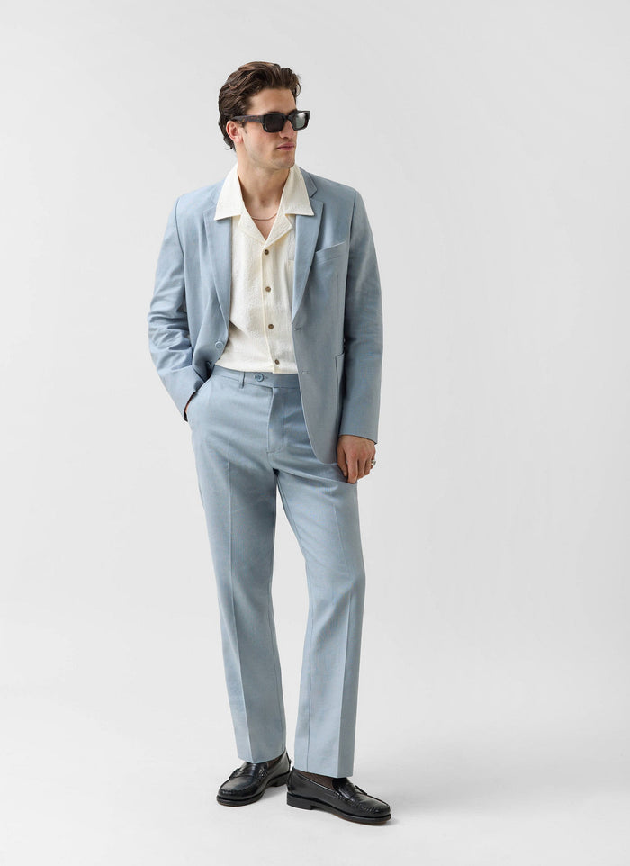 Model wears the Percival light blue linen suit with a cream shirt, black loafers and sunglasses.