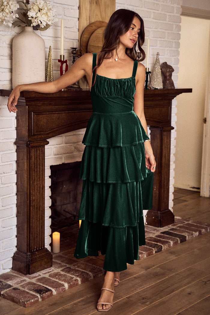 Woman in a green velvet dress standing in front of a fireplace.
