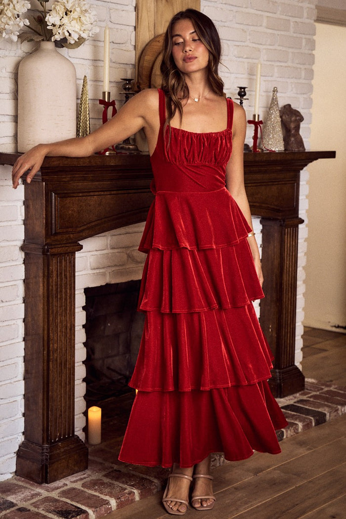 Woman in a red velvet dress standing in front of a fireplace.