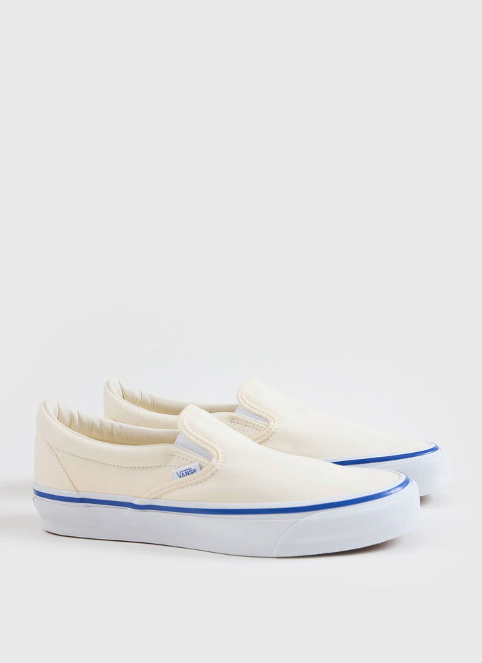 A side view of the Vans Slip-On Reissue 98 Shoes in off white canvas with a blue contrast stripe, from Percival.